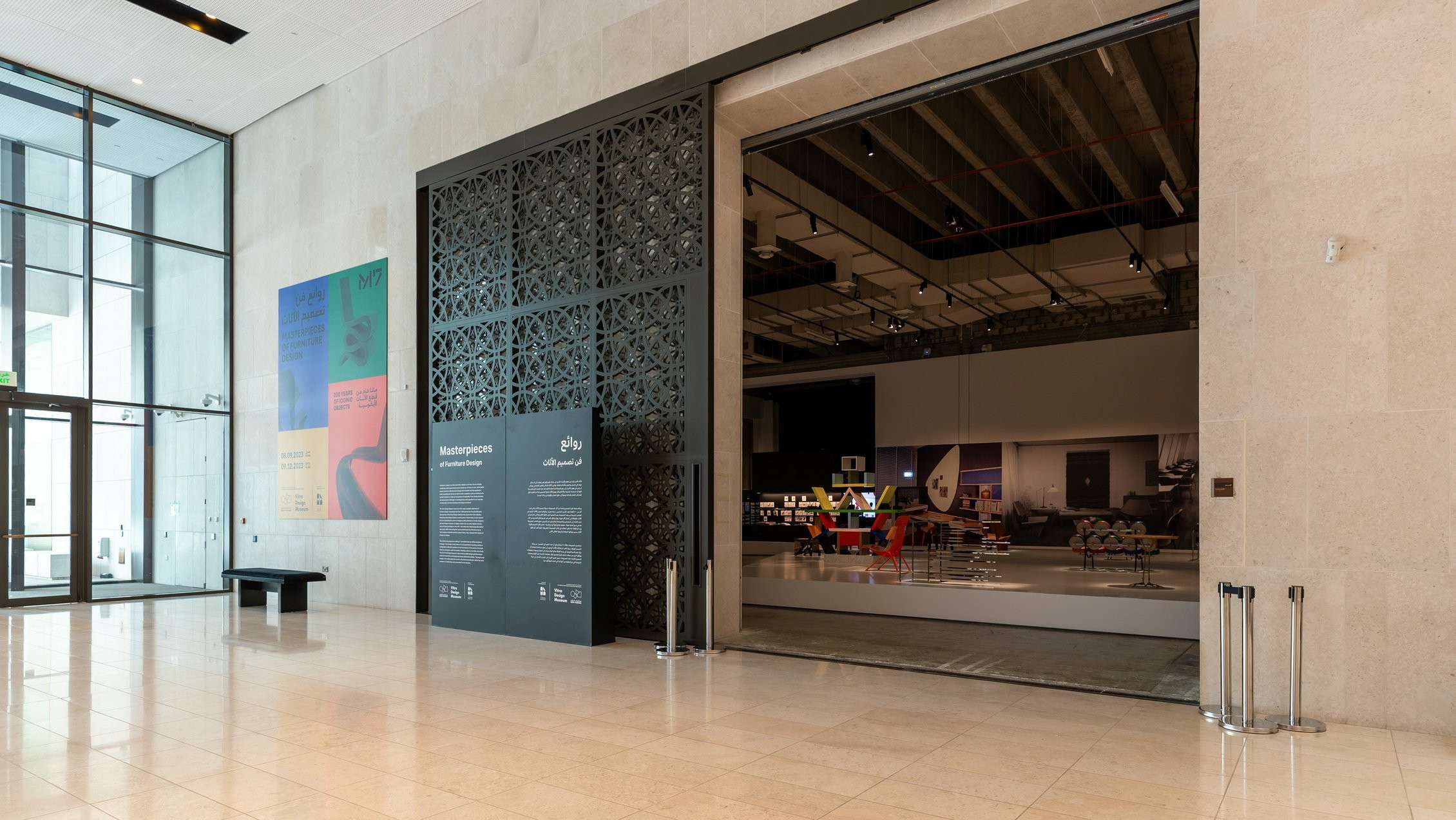 A modern museum entrance at M7 Msheireb Downtown featuring large glass walls, decorative black panels, and colorful exhibit posters.