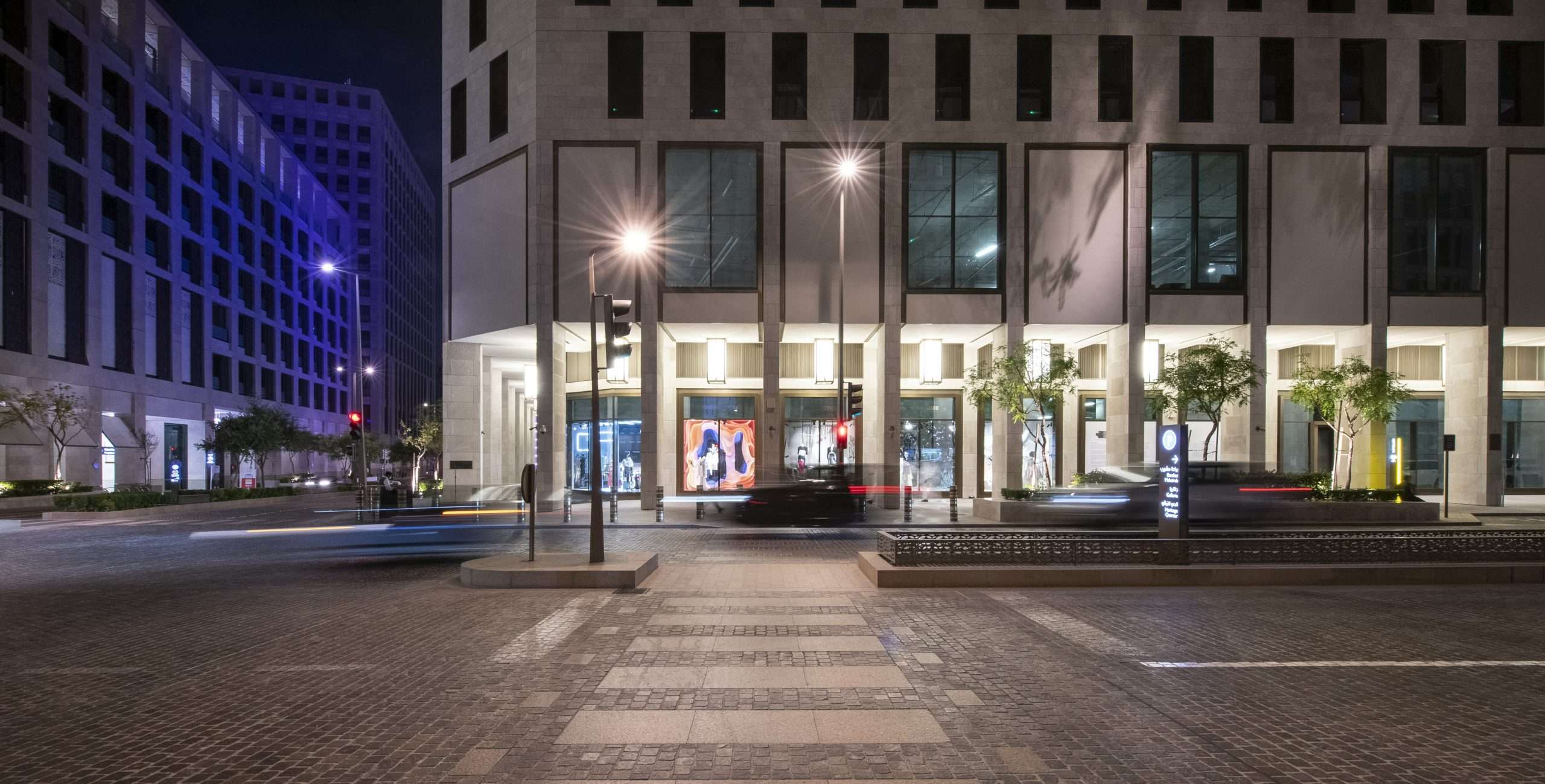 A modern building at night with bright lights, traffic, and trees in view in Msheireb Downtown